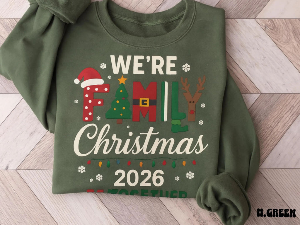 Green sweatshirt with Christmas-themed text and graphics on a wooden floor.