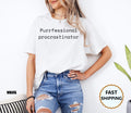 White: Woman wearing a white t-shirt with black text reading Purrfessional procrastinator