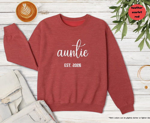 Heather scarlet red Auntie Est 2026 sweatshirt folded on a wooden table next to coffee and leaves