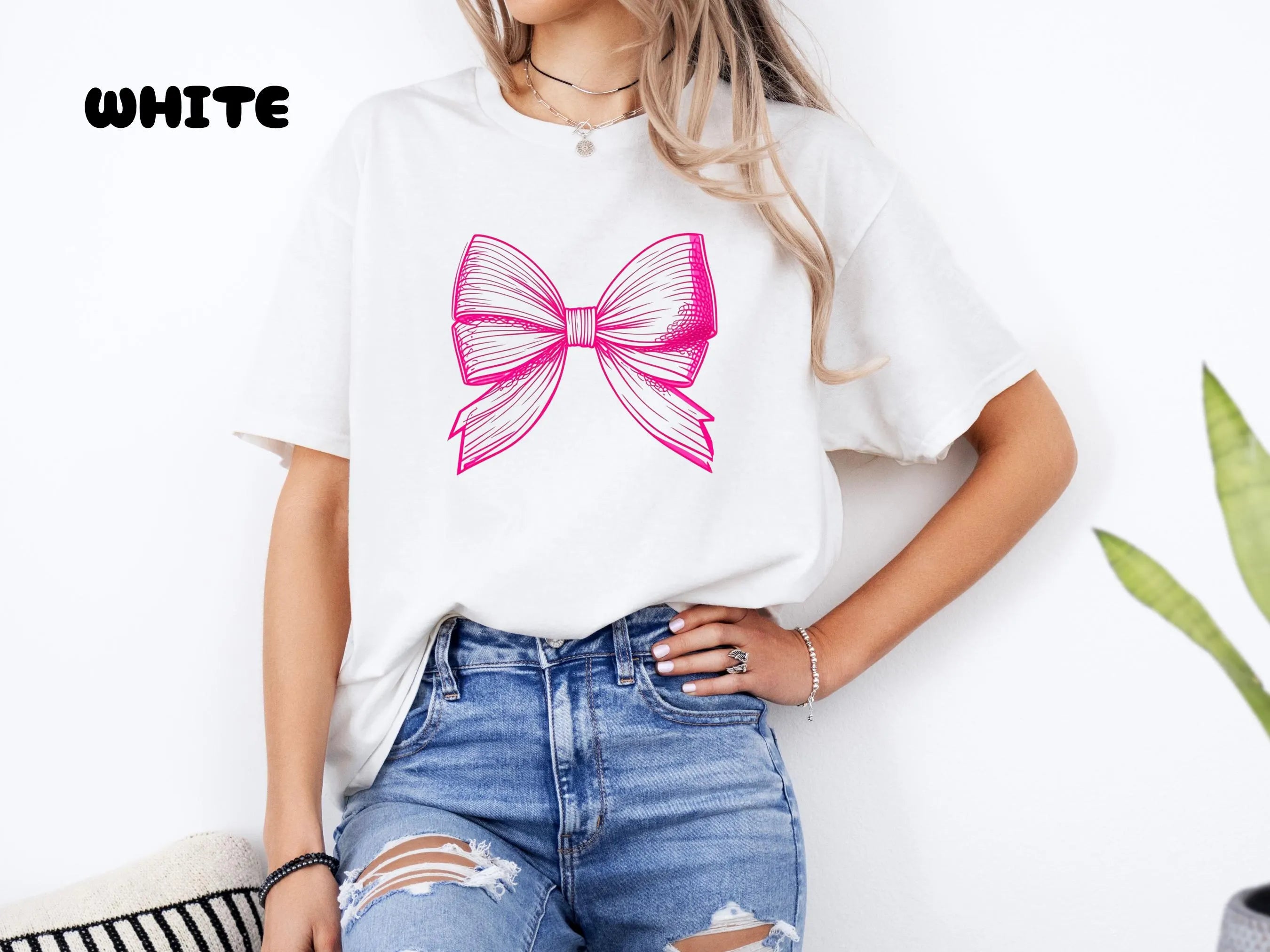 Person wearing a white t-shirt with a pink bow design and ripped jeans.