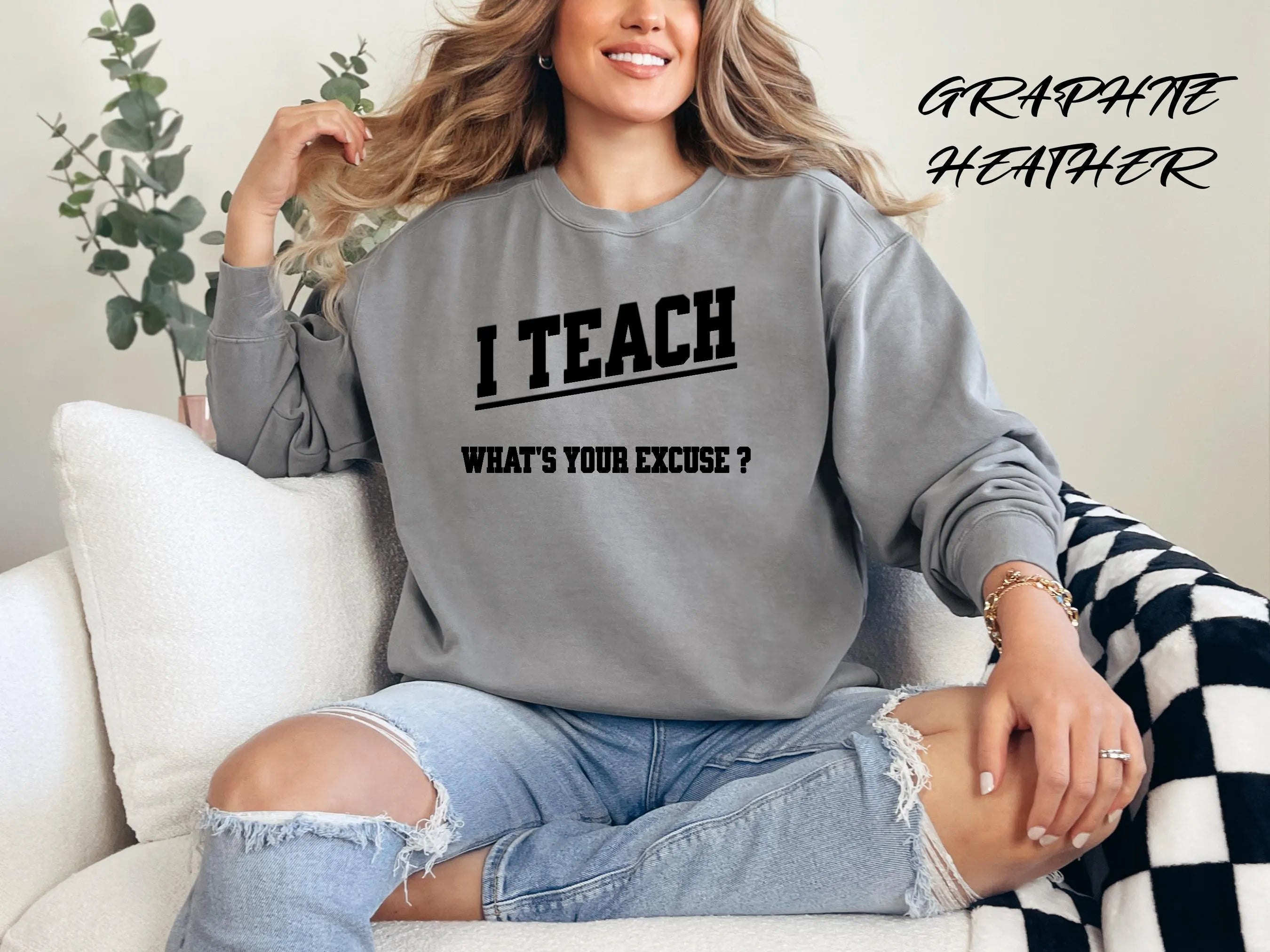 Woman wearing a gray sweatshirt with 'I TEACH WHAT'S YOUR EXCUSE?' text, sitting on a couch.