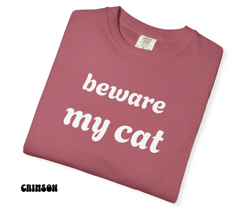 Folded pink t-shirt with 'beware my cat' text on a white background