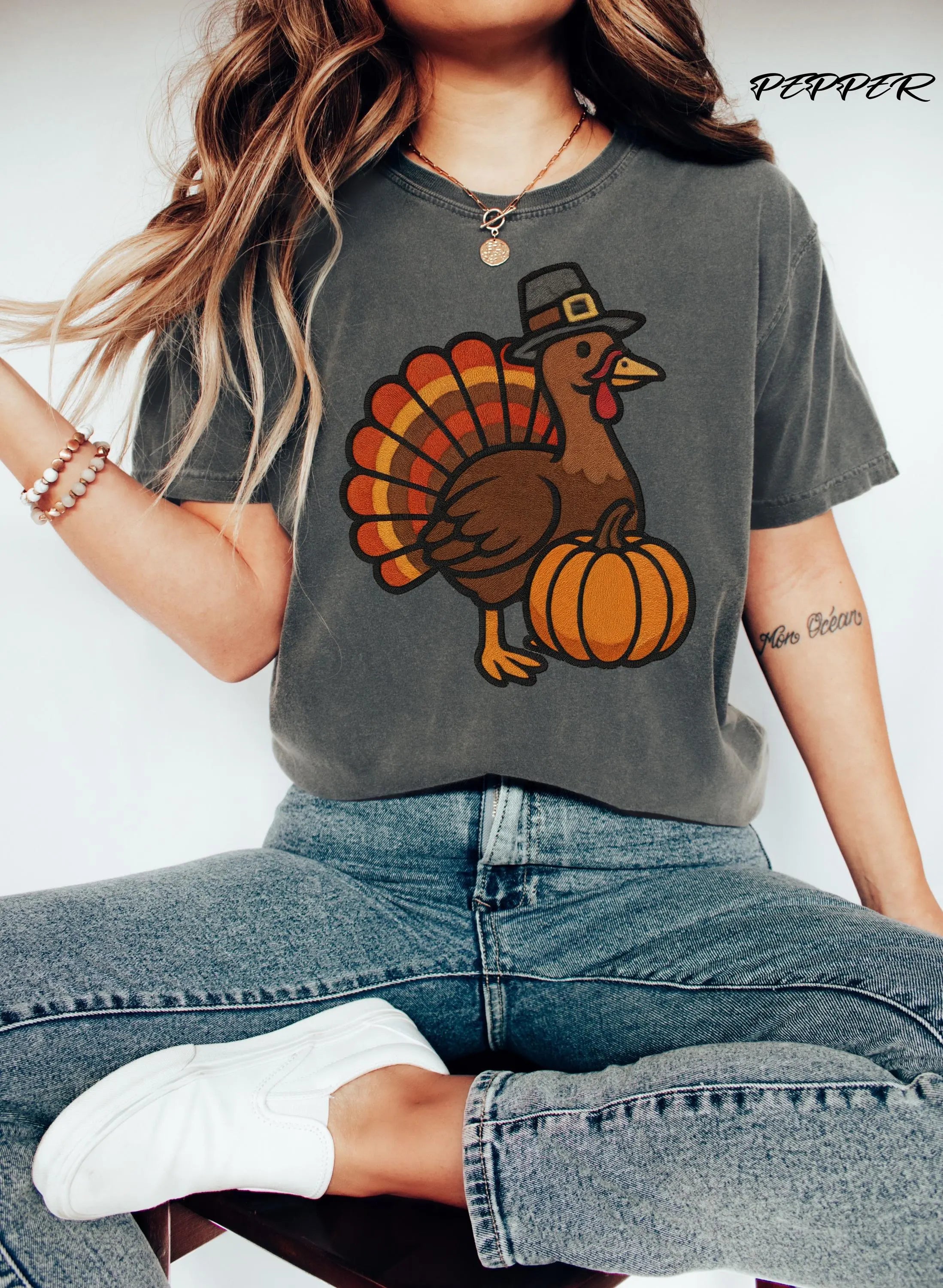Person wearing a gray t-shirt with a turkey and pumpkin design, sitting on a white background.