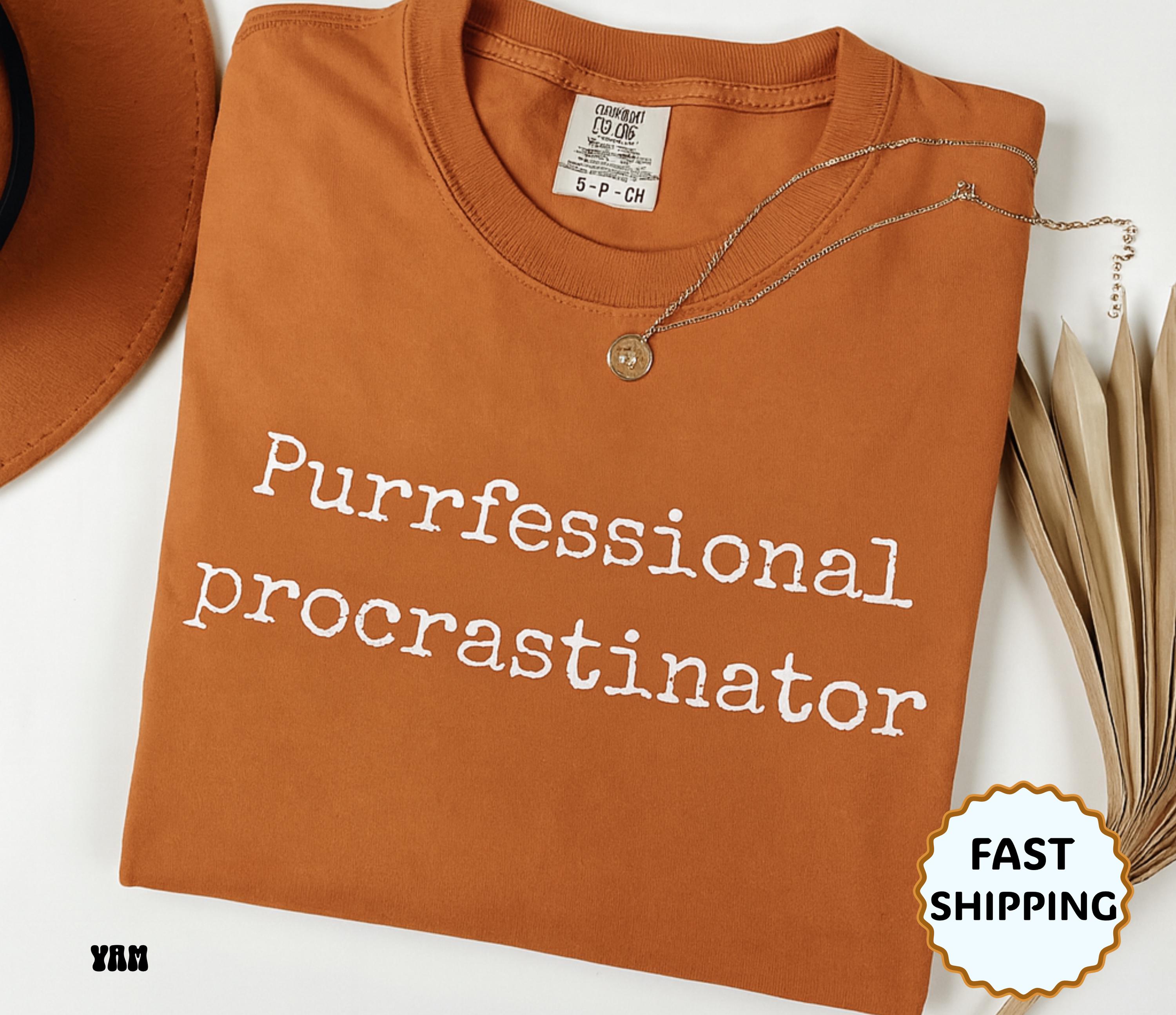 Folded orange t-shirt with 'Purfessional procrastinator' text on a white background