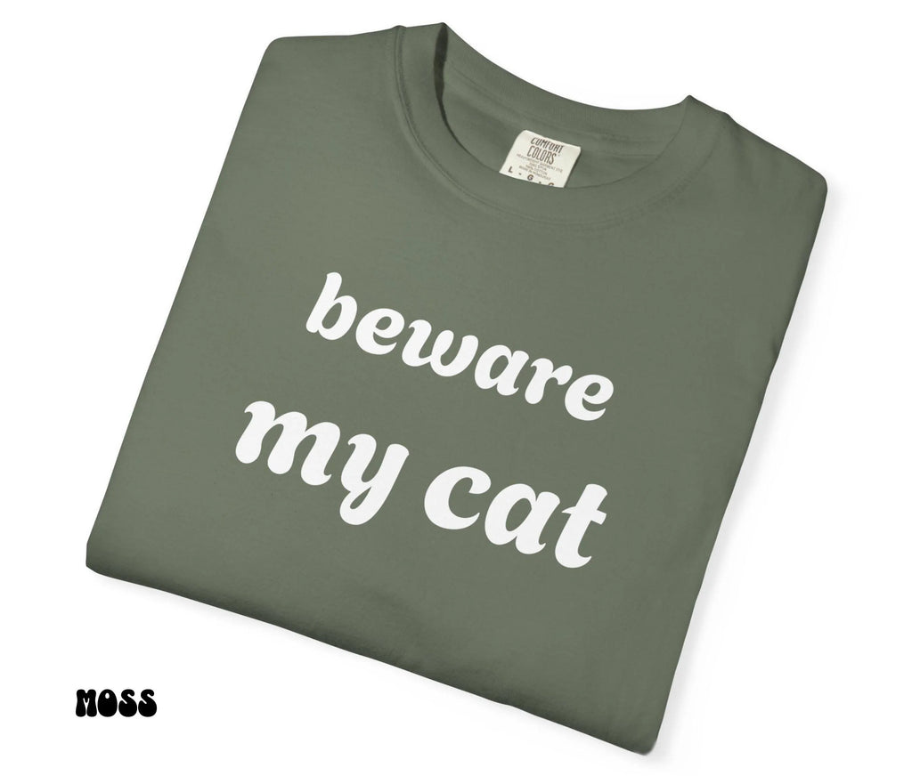 Folded green t-shirt with 'beware my cat' text on a white background