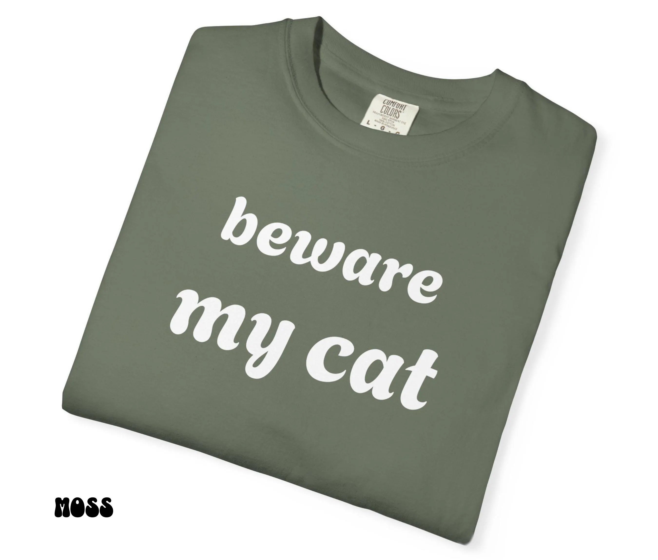 Folded green t-shirt with 'beware my cat' text on a white background